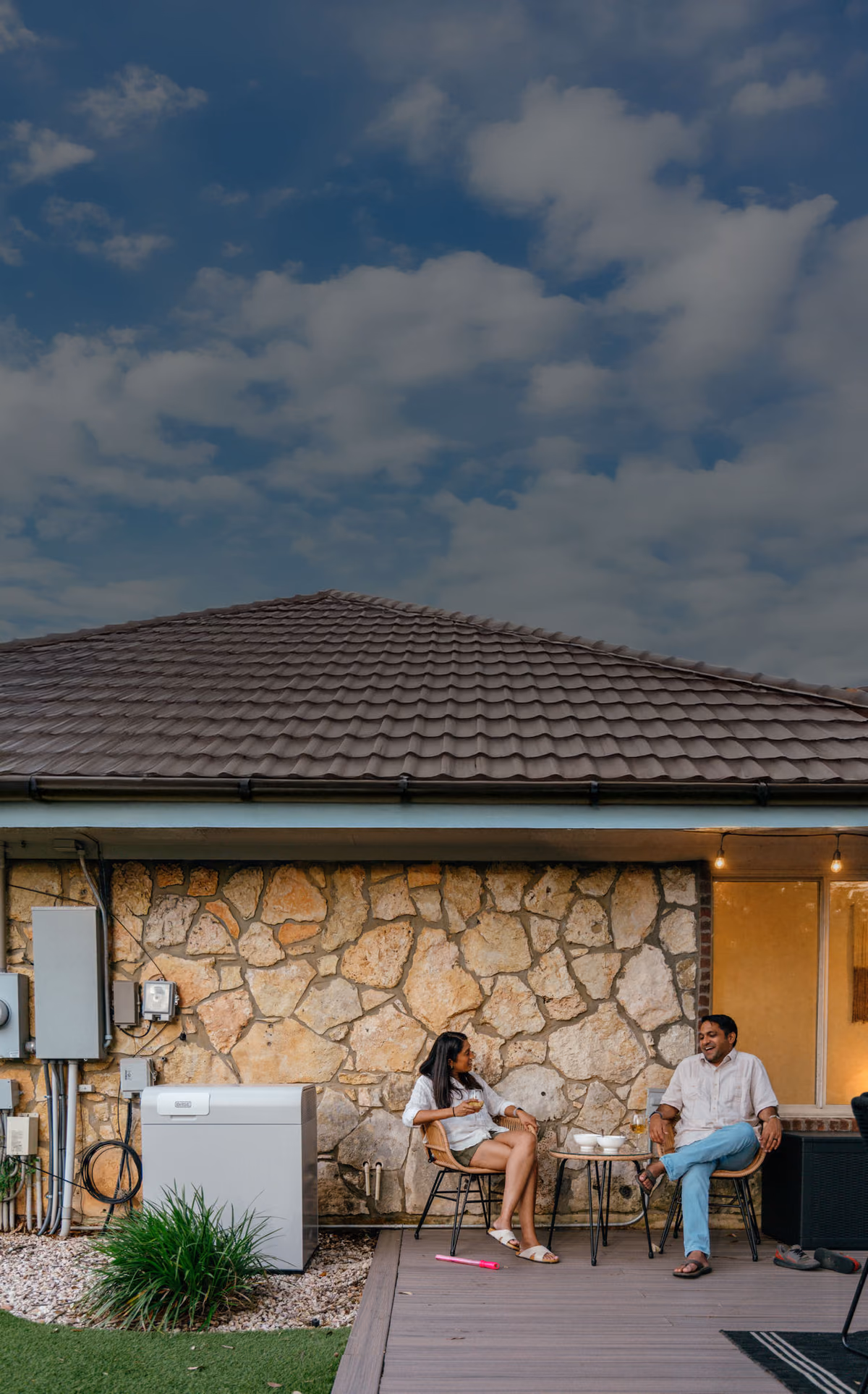 A couple relaxing on a patio beside a Base Power battery at dusk