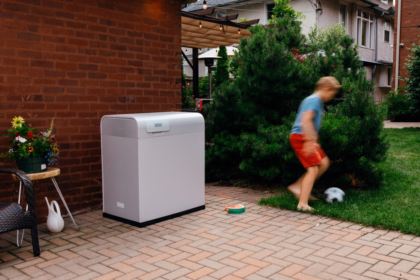 A child playing soccer in a backyard beside a Base Power battery