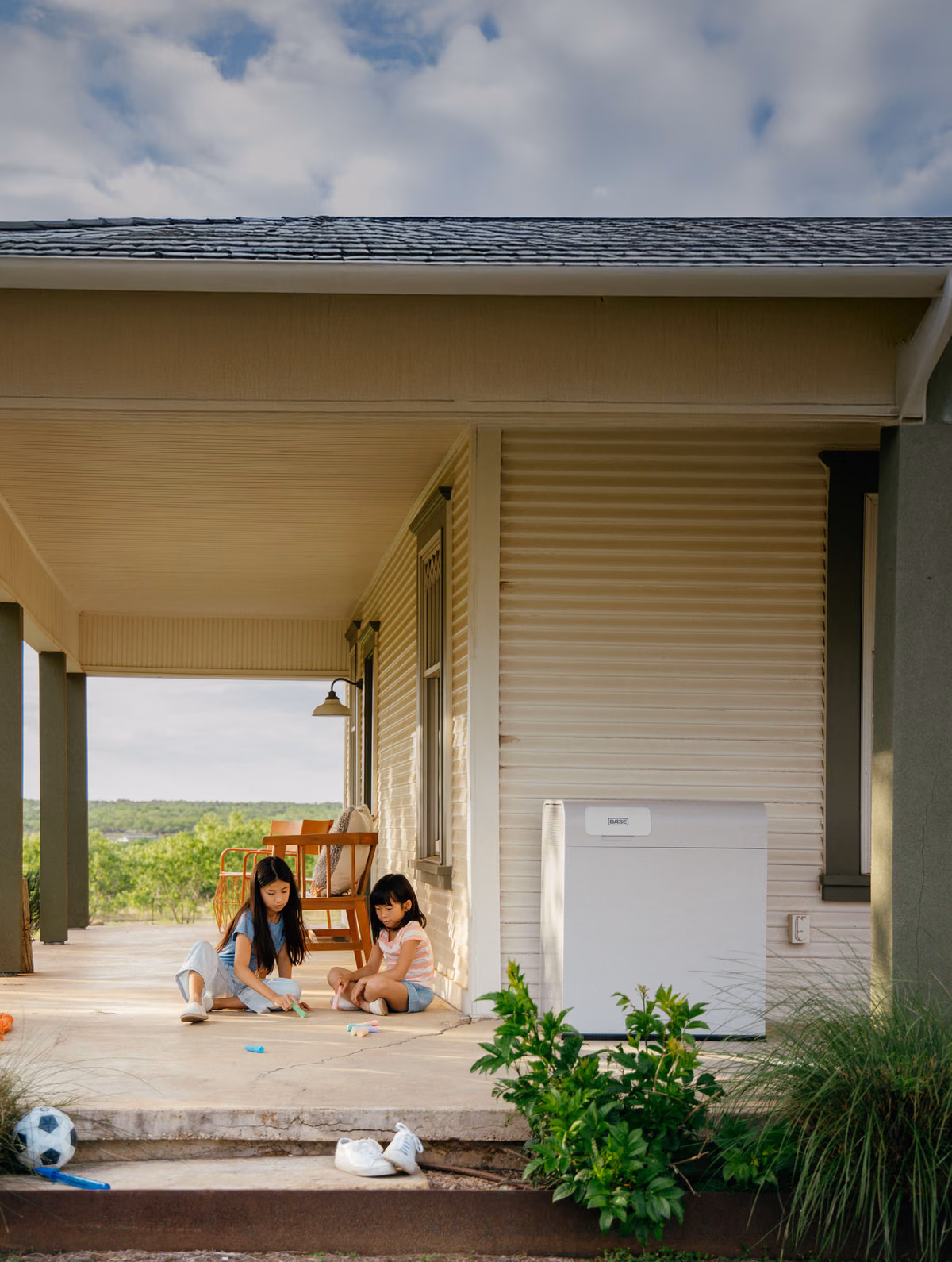 Two children playing on a porch beside a Base Power battery