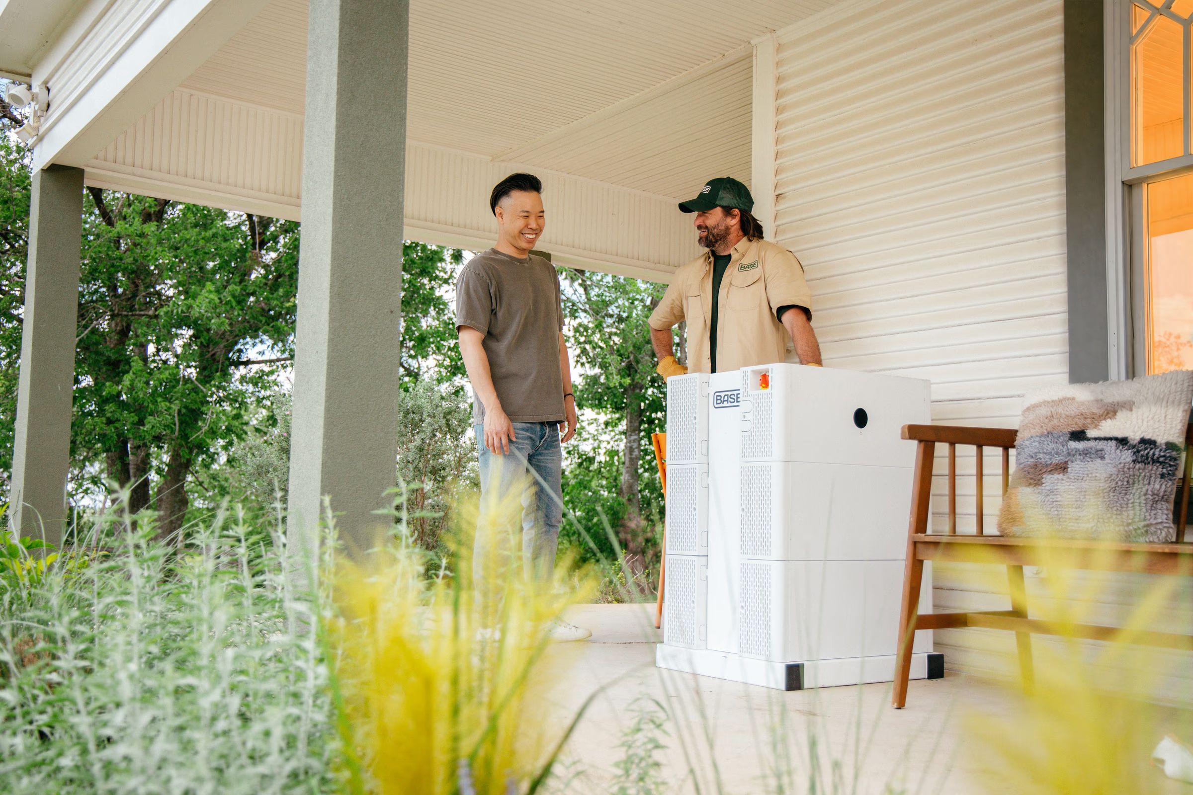 Two men smiling on a porch beside a Base Power battery installation