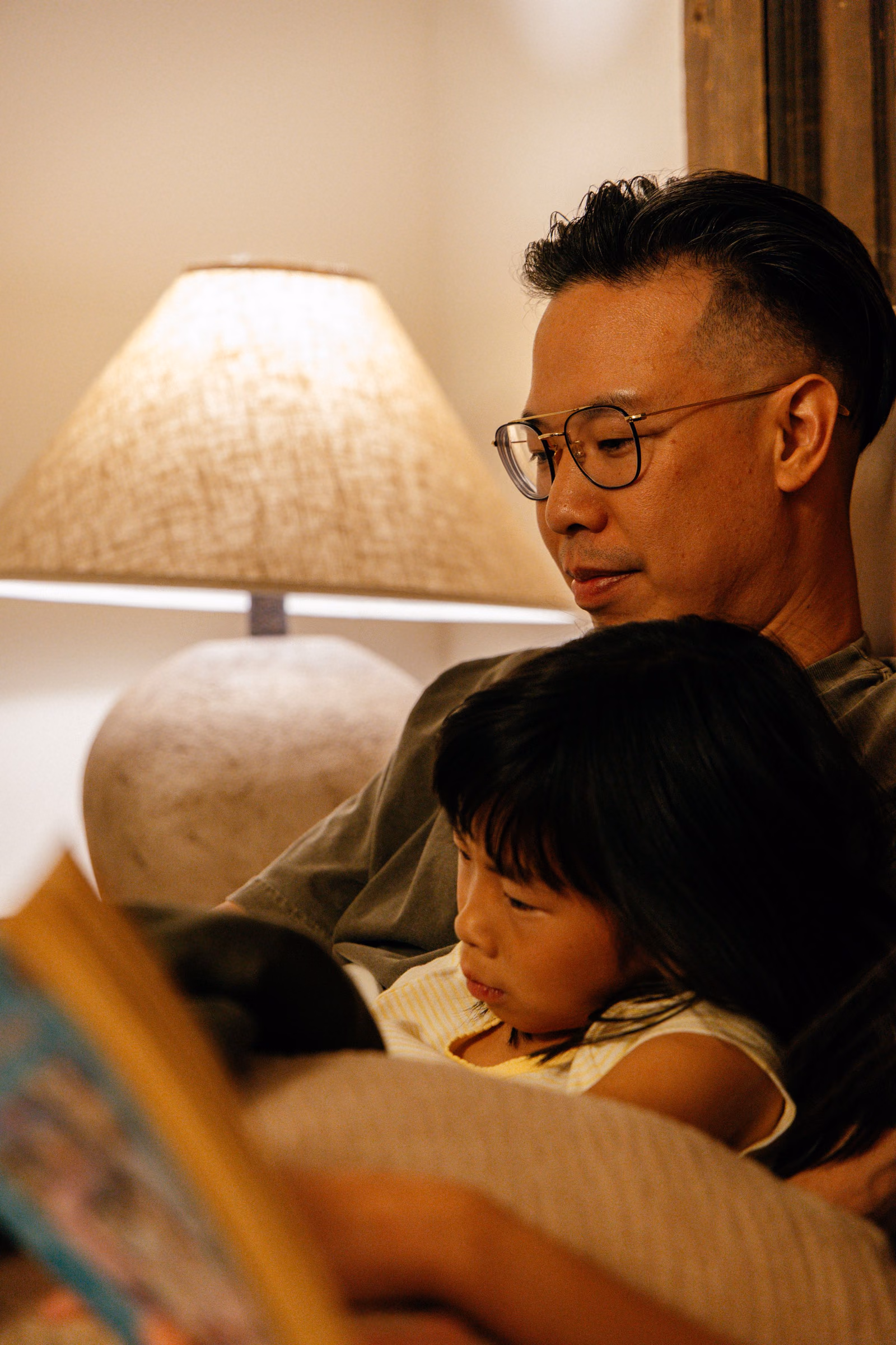 A parent reading to a child by lamplight at home